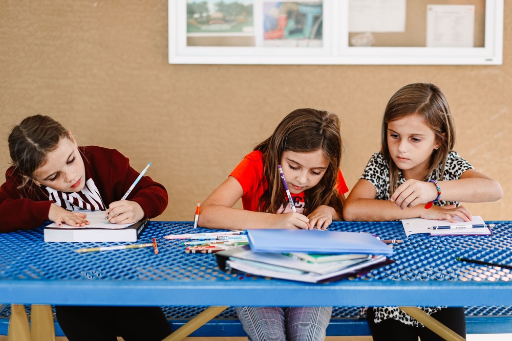 Three girls writing at a picnic table